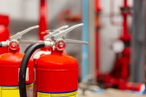 Close-up of red fire extinguishers with focus on the nozzle and safety pin, set against a blurred background, highlighting NY Fire Protection Services Long Island for optimal safety and preparedness.